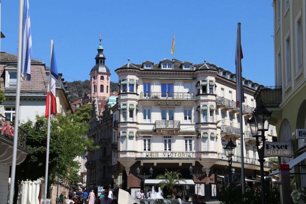Prächtiges mehrstöckiges Jugendstilgebäude mit Balkonen und Schriftzug "Haus Victoria" an einer belebten Fußgängerstraße bei blauem Himmel.