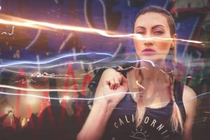 Junge Frau mit geflochtenen Haaren und schwarzem Tanktop vor neonbeleuchtetem, verschwommenem Konzert- oder Clubhintergrund, Lichtspuren ziehen quer durchs Bild.