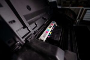 Offener Tintenstrahldrucker mit sichtbaren CMYK-Tintenpatronen in einer Reihe, Innenmechanik und Papierführung sichtbar.