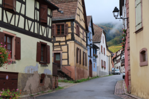 Enge Dorfstraße mit historischen Fachwerkhäusern und Nebel im Hintergrund