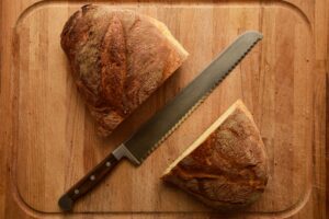 Gekreuzter Brotmesser auf einem Schneidebrett neben zwei Brotstücken