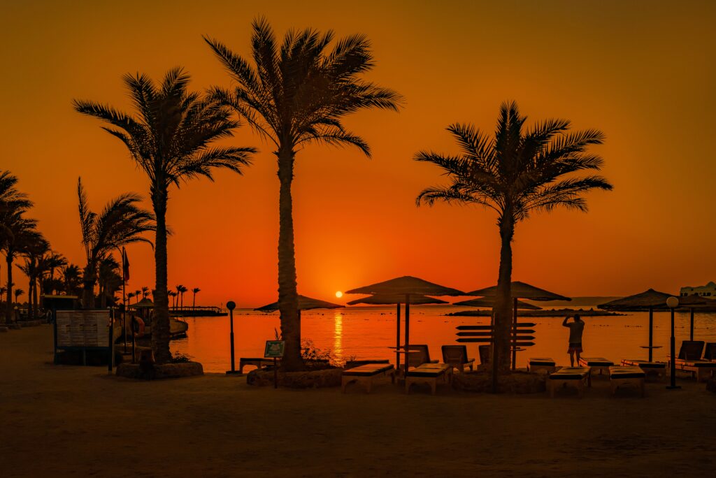 Sonnenuntergang am Strand mit Palmen, Liegen und Sonnenschirmen am ruhigen Meer