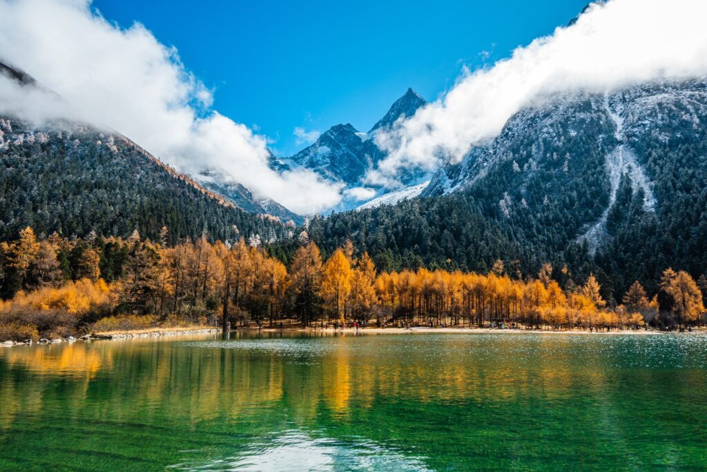 Bergsee vor schneebedeckten Gipfeln und herbstlichen Lärchen im Tal