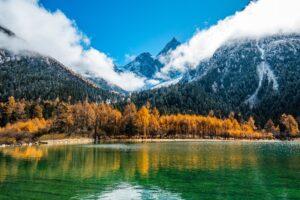 Bergsee vor schneebedeckten Gipfeln und herbstlichen Lärchen im Tal