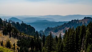 Blick über bewaldete Bergkämme und ein tiefes, nebliges Tal mit einer Serpentinenstraße