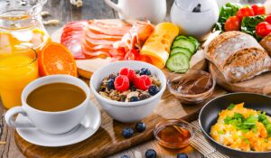 Frühstückstisch mit Kaffee, Orangensaft, Müsli, Brot, Käse, Aufschnitt, Eiern und frischem Obst und Gemüse
